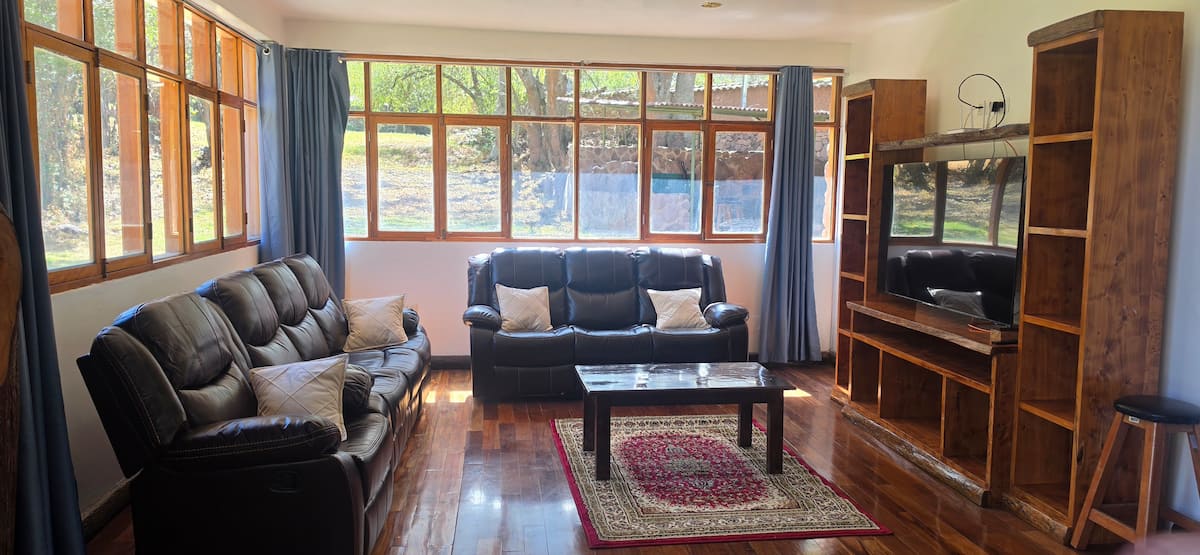 Sala principal con sofás de cuero, TV y ventanales al jardín